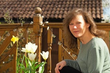 Çiçekli nergisler ve lalelerle dolu bir konteynerin yanında çekici bir esmer resmedilmiş..