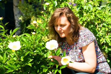 Mutlu bir gülümseme ve çekici olgun bir esmer göstermek, çiçek açan şakayık tomurcuğu tutmak, Haziran başında.