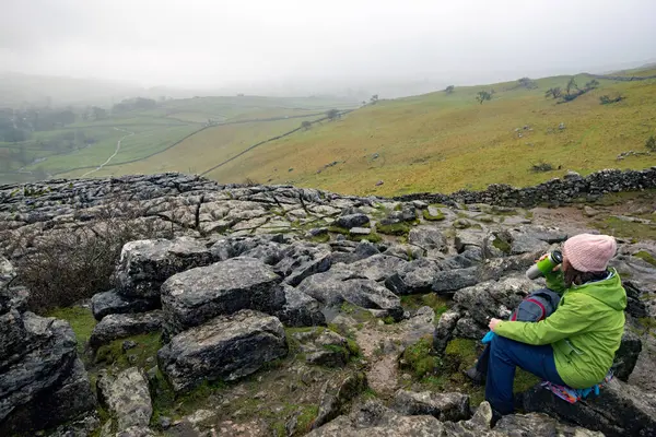 A bag for life makes for an ideal seat on the very wet and rugged terrain of Malham Cove, in January 2024.