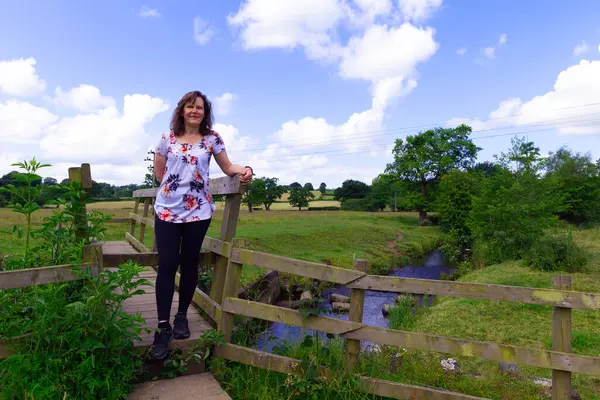 Stretton, Derbyshire 'da, ahşap bir köprünün yanında, eğlenceli bir yürüyüş yapan çekici, olgun bir esmer kadını yakalamak..