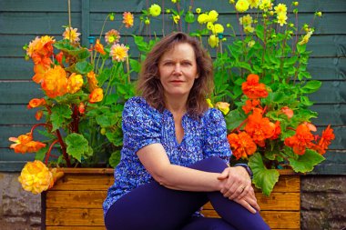 Güzel ve mutlu bir esmer bayanı büyük bir begonya ve pom pom dahlias koleksiyonunun yanında yakalıyorum..