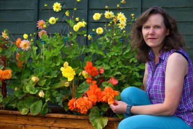 Güzel ve mutlu bir esmer bayanı büyük bir begonya ve pom pom dahlias koleksiyonunun yanında yakalıyorum..