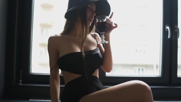 穿着性感黑衣坐在窗边喝红酒 动作缓慢的年轻貌美女人 — 图库视频影像