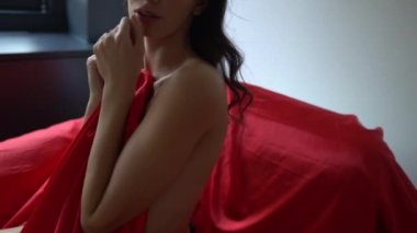 Göğüslerini kırmızı satenle kaplayan ve kameraya şehvetli pozlar veren genç seksi kadın, ağır çekim.