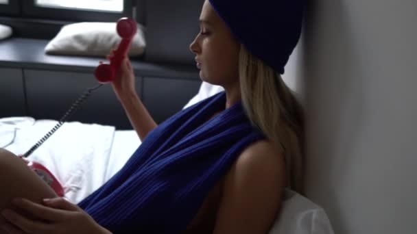 年轻性感金发女人半裸着身子 慢吞吞地坐在床上 拿起红色旧旋转电话的耳机 — 图库视频影像