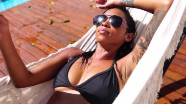 Siyah bikinili seksi genç kadın havuz başındaki hamak yatağında dinleniyor, 4K yakın çekim.