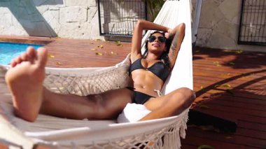 Siyah Bikinili Genç Seksi Kadın Havuz kenarında uzanıyor ve Müzik 4k 'nin tadını çıkarıyor.