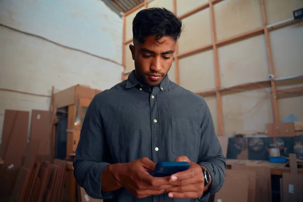 Odaklanmış Gömlekli Genç Adam Ahşap Fabrikasındaki Odunları Cep Telefonuyla Kullanıyor — Stok fotoğraf