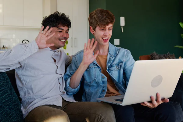 在家里客厅里 一对快乐的年轻同性恋夫妇在笔记本电脑上的视频通话中挥手微笑 — 图库照片