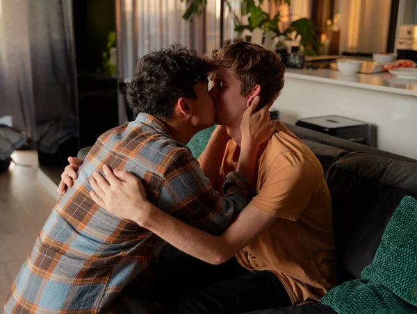 stock image Young gay couple in casual clothing kissing during reconciliation on sofa in living room at home