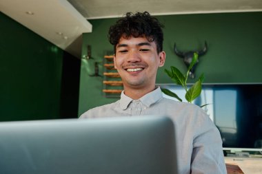 Evdeki oturma odasında dizüstü bilgisayar kullanırken gülümseyen çok ırklı bir adamın seçici odağı.