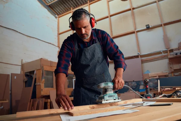 耳のマフを着用し 木工工場で木板の上のパワーツールを使用して多人種中大人の男 — ストック写真