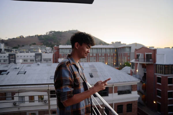日落时分 穿着衬衫的多种族年轻人在公寓阳台上使用电话的简况 — 图库照片
