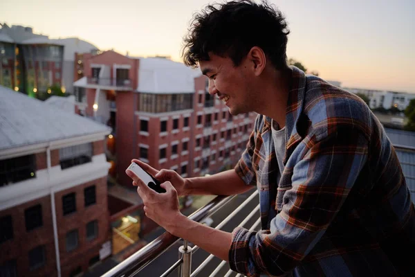 Happy Young Multiracial Man Checkered Shirt Using Phone Balcony Apartment — Stock Photo, Image