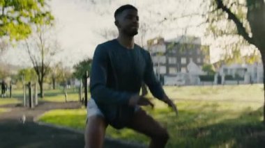 Spor kıyafetli atletik bir genç adam parktaki kaldırımda çömeliyor ve zıplıyor.