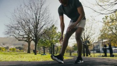 Spor elbiseli atletik genç siyah adam parkta kaldırımda ısınma egzersizleri yapıyor.