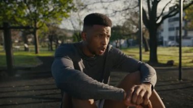 Spor elbiseli genç bir zenci parkta cep telefonu kullanırken ara veriyor ve gülümsüyor.