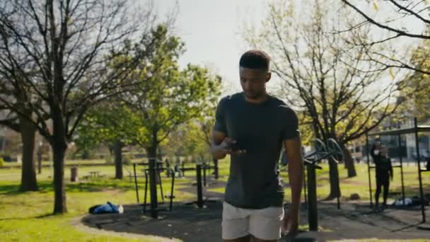 Spor Giyimli Genç Bir Adam Parkta Yürürken Gülümsüyor Cep Telefonuyla — Stok video