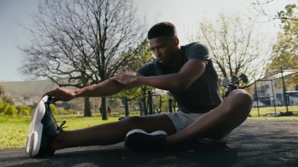 身穿运动服的年轻黑人运动员坐在公园的人行道上做伸展运动 — 图库视频影像