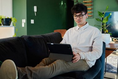 Gömlekli genç adam dijital tablet kullanıyor. Kablosuz kulaklık takıyor.