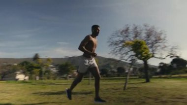 Parkta spor antrenmanı sırasında şortlu genç bir adam ileri geri koşuyordu.