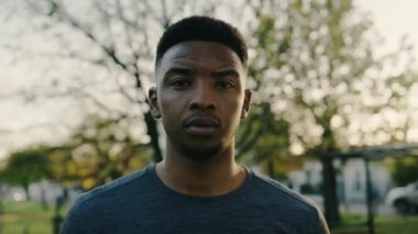 Parkta ağaçların arasında mola verirken kameraya bakan siyahi bir adamın portresi.