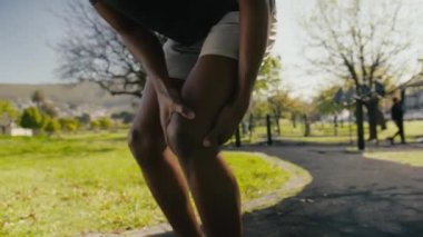 Spor elbiseli atletik genç siyahi adam parkta kaldırımda dizlerini uzatıyor.