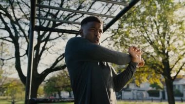 Spor elbiseli kararlı genç bir zenci parkta ağaçların arasında maymun parmaklıklarının altında geriniyor.