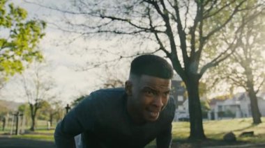 Spor kıyafetli genç bir zenci parkta kaldırımda ağırlık kaldırarak şınav çekiyor.