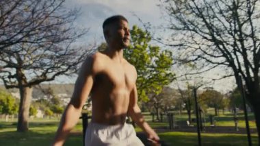 Atletik tişörtsüz genç siyah adam parkta ip atlama egzersizi yapıyor.