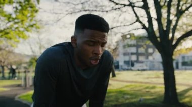 Spor kıyafetleri içinde genç bir adam ara verdiğinde ağaçların parkta yaptığı egzersizler arasında nefes veriyor.