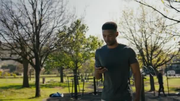 Ung Svart Man Sportkläder Ler Och Använder Mobiltelefon När Går — Stockvideo