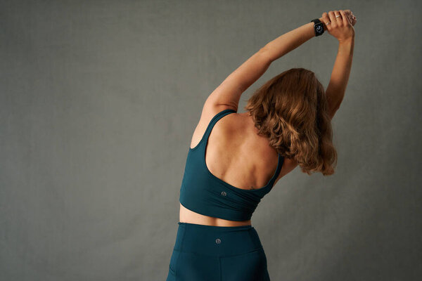 Rear view of young caucasian woman wearing sports clothing with arms raised while stretching in studio