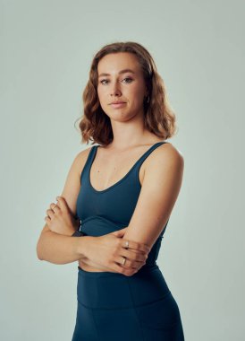 Three quarter portrait of young caucasian woman wearing sportswear looking at camera with arms crossed
