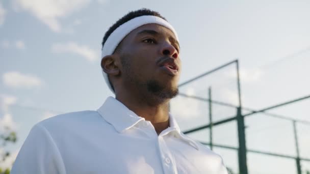 年轻的黑人男子头戴发带 一边在运动场上玩游戏一边用网球拍呼气 — 图库视频影像