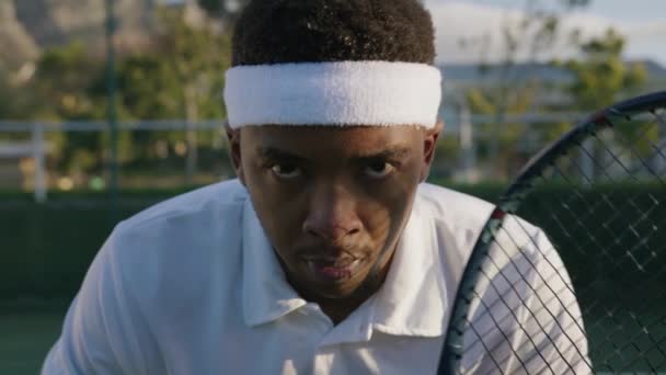 スポーツコートでプレーしながら テニスラケットでヘッドバンドを身に着けている若い黒人男性に焦点を当て — ストック動画