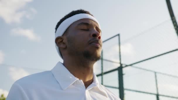 年轻的黑人男子身穿运动服 一边在运动场休息 一边用网球拍大呼小叫 — 图库视频影像