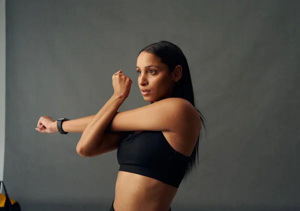 Determined young biracial woman wearing sports bra doing cross arm stretch in studio