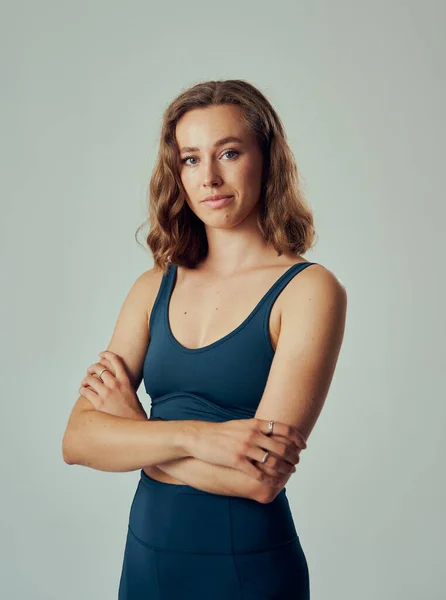 Confident young caucasian woman wearing sportswear looking at camera with arms crossed in studio