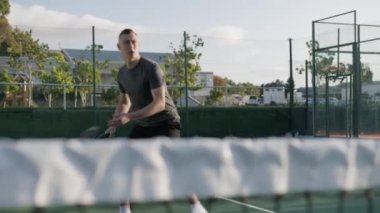 Spor giyim sektöründe genç bir adam tenis kortunda tenis antrenmanı sırasında ağ üzerinden tenis topuna vuruyor.