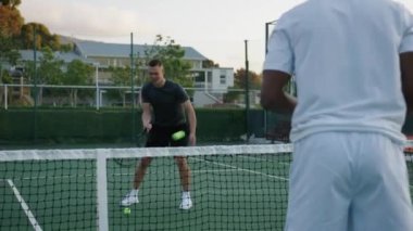 Young men wearing sportswear hitting tennis ball over net during tennis practice at sports court