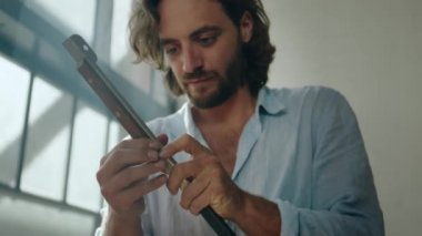 Ofisteki pencerede mal tutarken gömlek giyen genç beyaz bir adam aşağıya bakıyor.