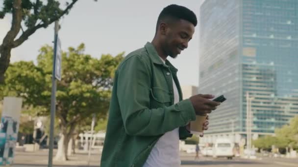携帯電話を使いながら笑顔でシャツを着た若い黒人男性と路上でコーヒーを飲みながら — ストック動画