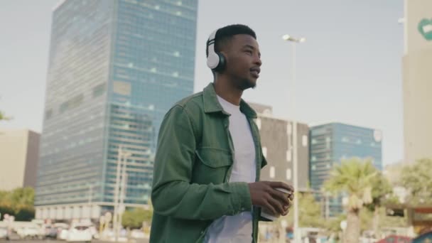 Młody Czarny Mężczyzna Koszuli Uśmiecha Się Podczas Autostopowiczów Słuchawkami Kawą — Wideo stockowe