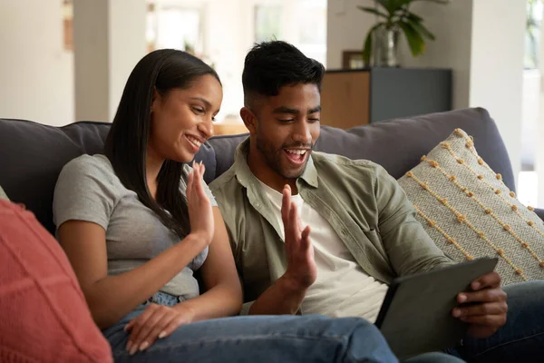 在家里的数码平板电脑上 快乐的年轻夫妇身着休闲装 一边在电视上挥手致意 — 图库照片