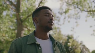 Parktaki ağacın altında nefes alıp verirken günlük giysiler giyen genç siyahi adamın portresi.