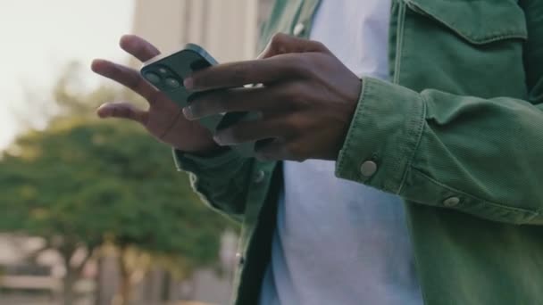 ストリートで携帯電話にスクロールカジュアル服を着て若い黒人男性のクローズアップ — ストック動画