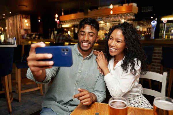 年轻的多种族夫妇穿着休闲装 面带微笑 在酒吧用手机自拍 — 图库照片