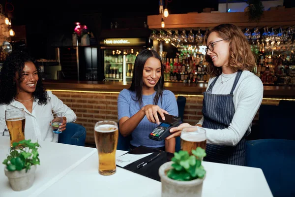 快乐的年轻女性穿着休闲装 在服务员旁边用卡机支付酒钱 — 图库照片