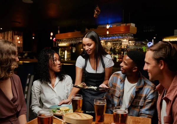 Happy young multiracial group of friends wearing casual clothing receiving dinner from waitress at bar
